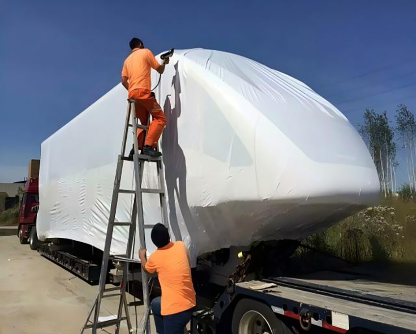 Workers wrapping large cargo on flatbed trailer for shipment transport